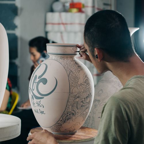 Free A craftsman delicately hand-paints a detailed design on a ceramic vase in Hanoi, Vietnam. Stock Photo