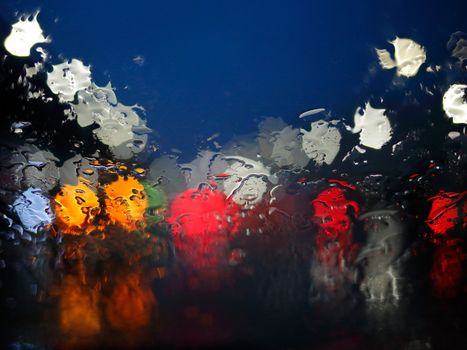 Abstract view of colorful city lights through a rain-soaked windshield on an evening in Dhaka.