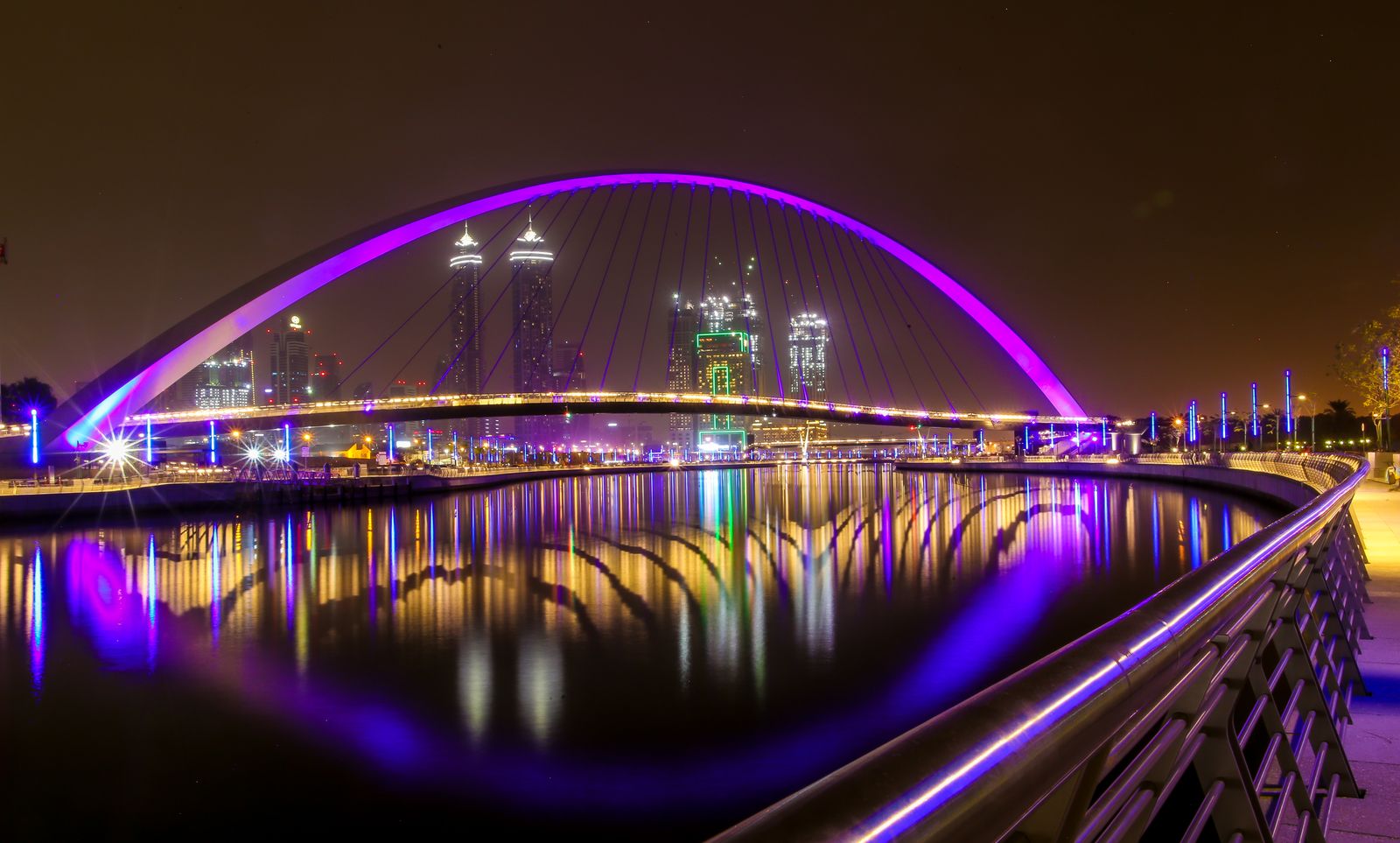 The Tolerance Bridge, the landmark arched pedestrian bridge over the Dubai Water Canal at Business Bay, illuminated at night with the district's towers behind.