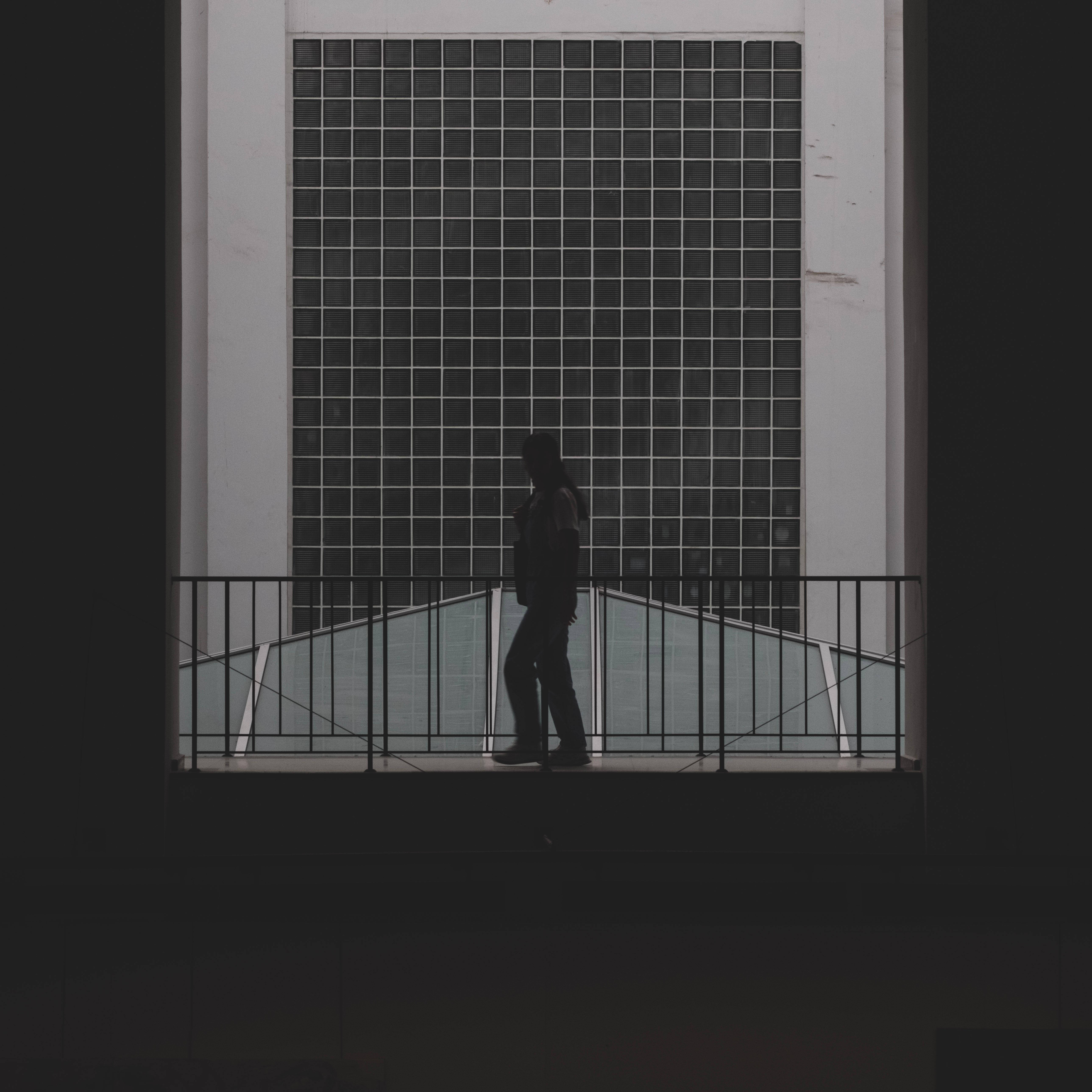 Silhouette of a person walking along a railing in front of geometric modern architecture.