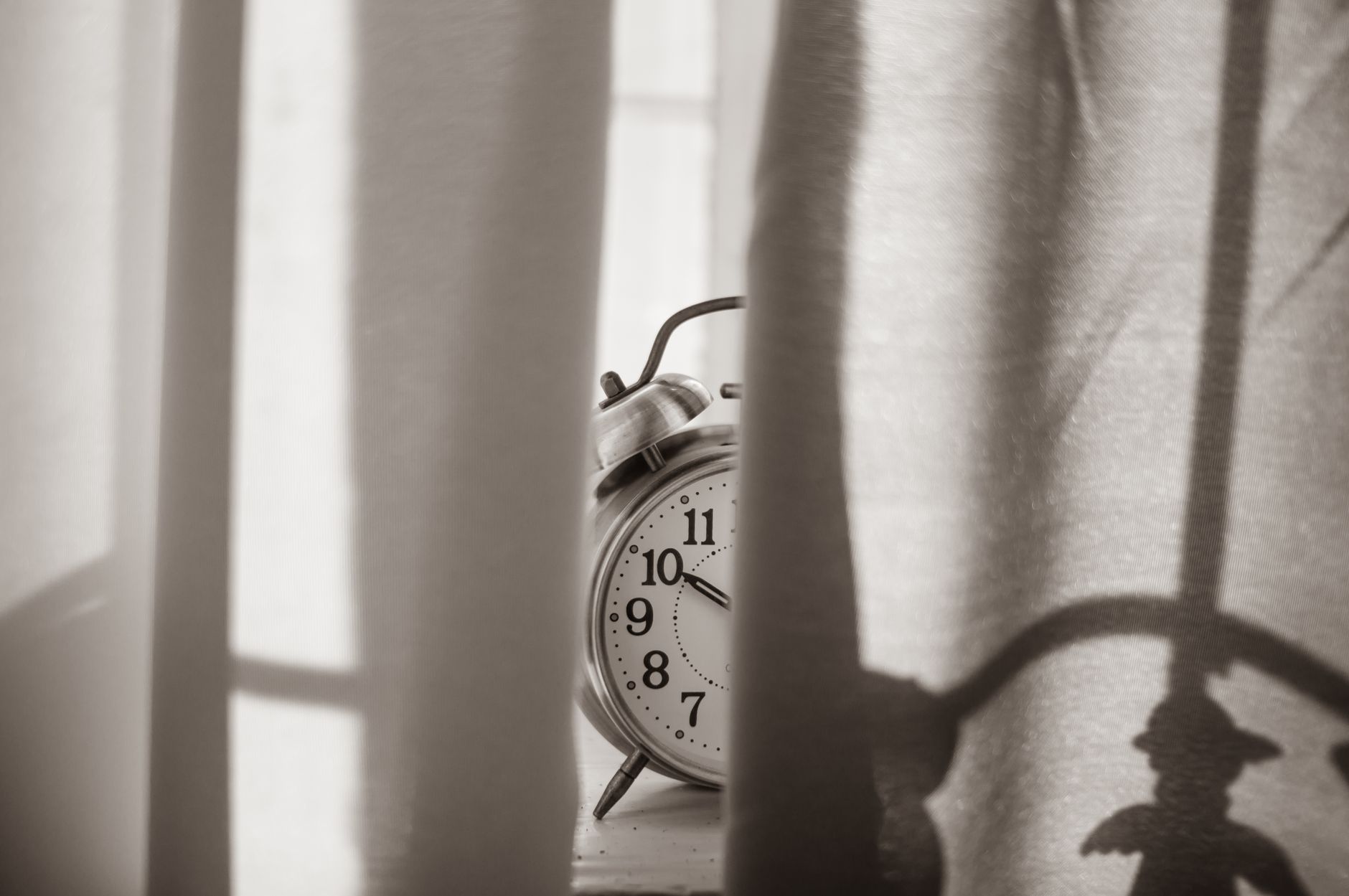 Monochromatic image of a vintage alarm clock peeking through curtains, conveying a sense of nostalgia.