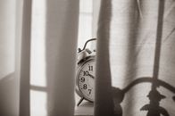 Monochromatic image of a vintage alarm clock peeking through curtains, conveying a sense of nostalgia.