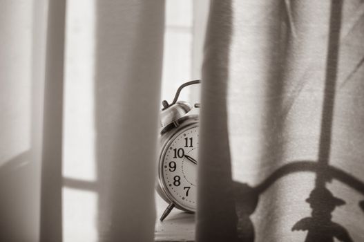 Monochromatic image of a vintage alarm clock peeking through curtains, conveying a sense of nostalgia.
