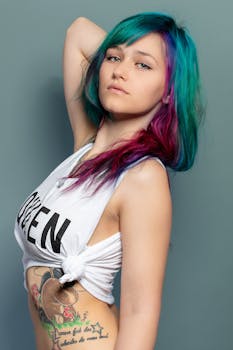 Young woman with colorful hair and tattoos posing in a studio setting.