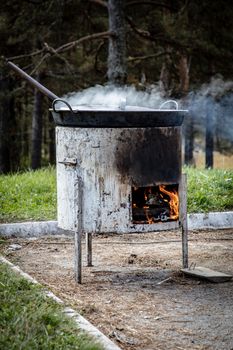 A rural outdoor scene of cooking over an open fire with visible flames and steam.