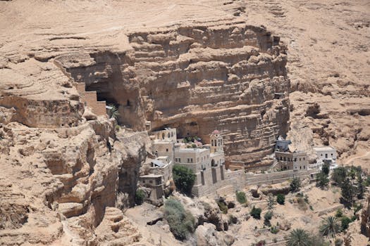 Aerial view of St George's Monastery nestled in the cliffs of Wadi Qelt, illuminated by bright sunlight.