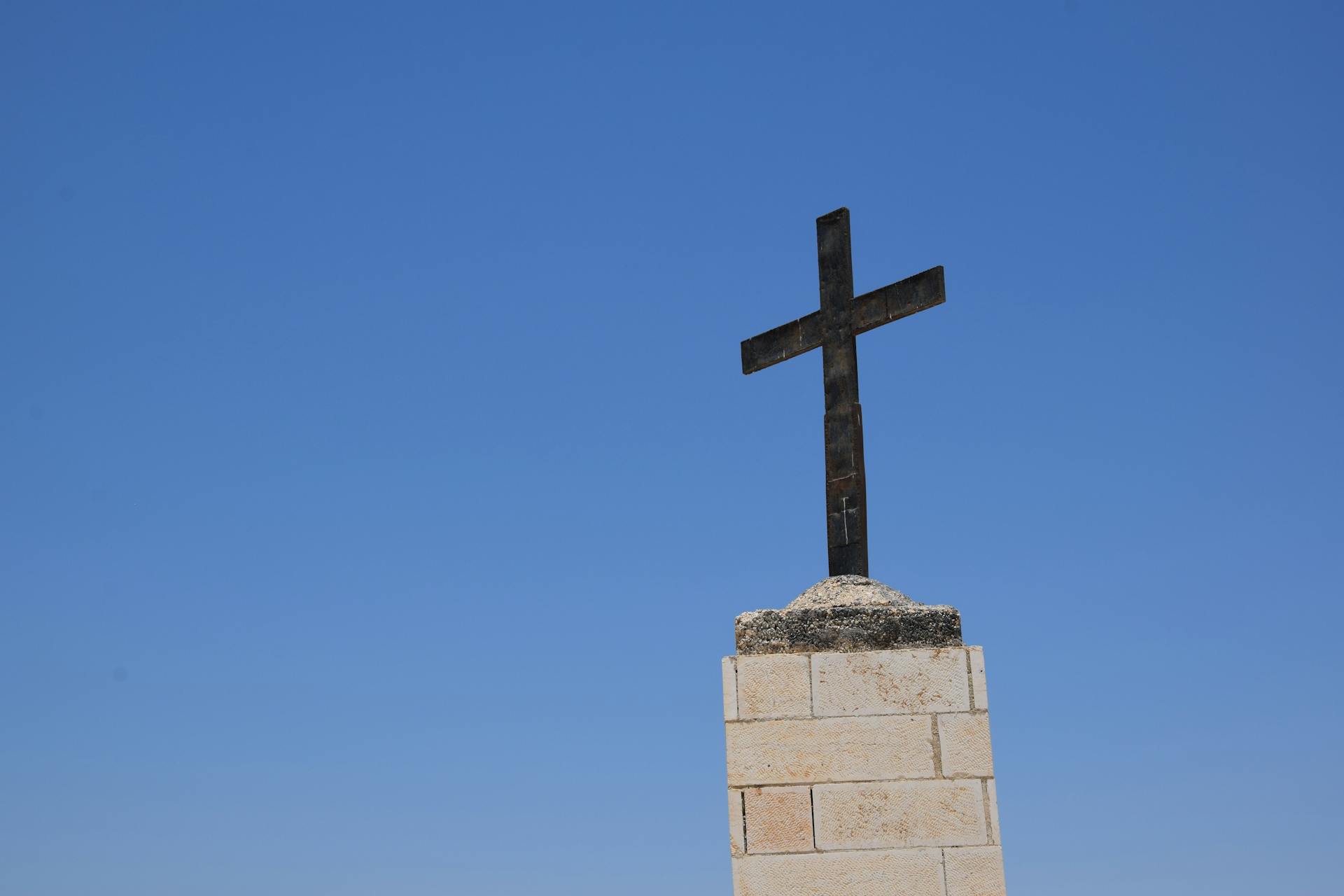 A solitary cross on a stone base stands tall against a vibrant blue sky, symbolizing faith and spirituality.