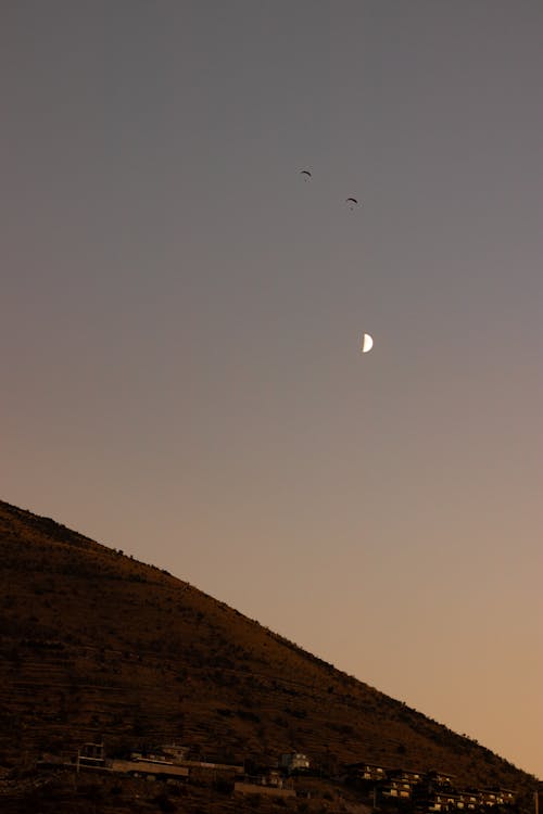People with Parachutes Falling on Mountainside at Dusk