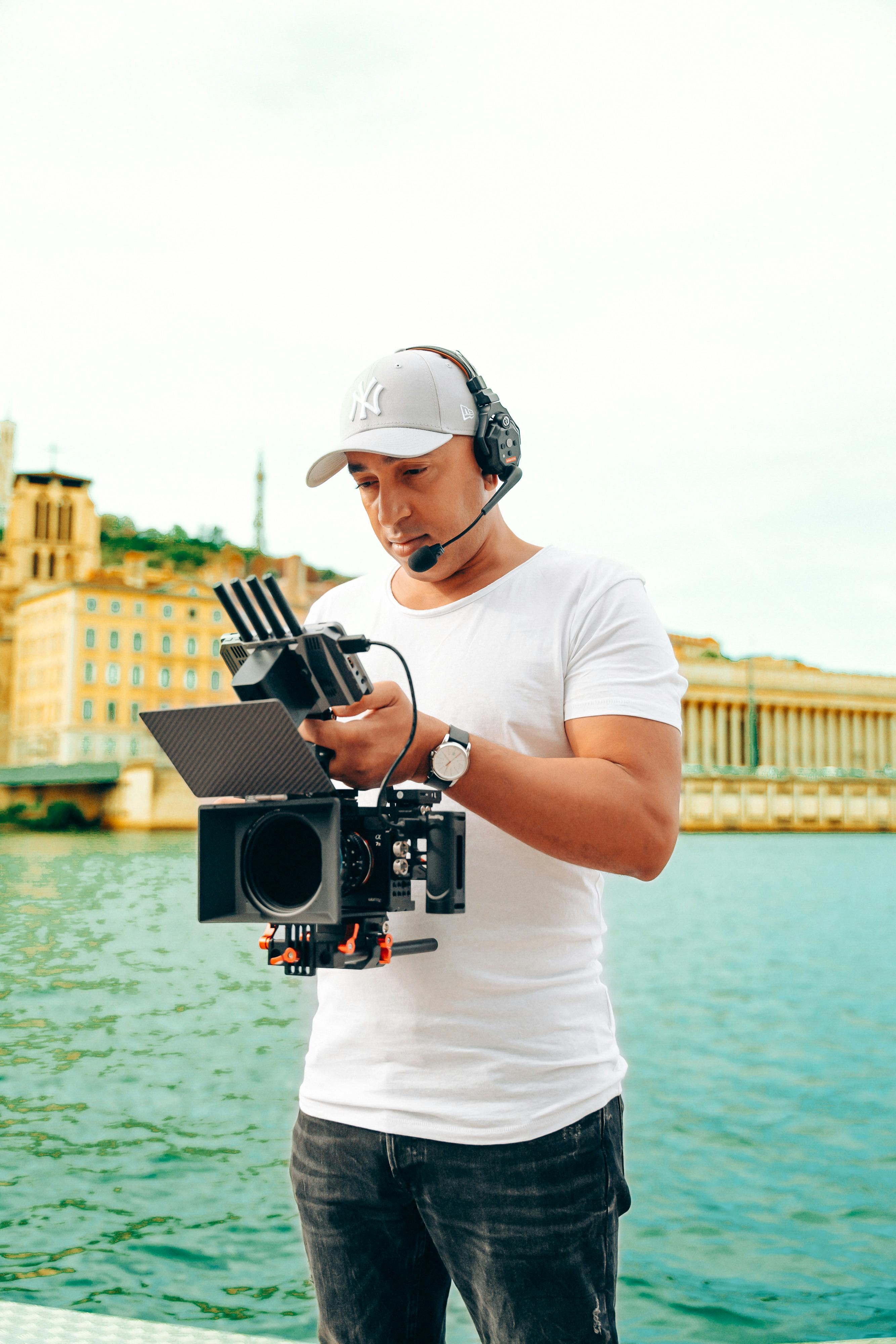 man in cap standing with camera by water in town