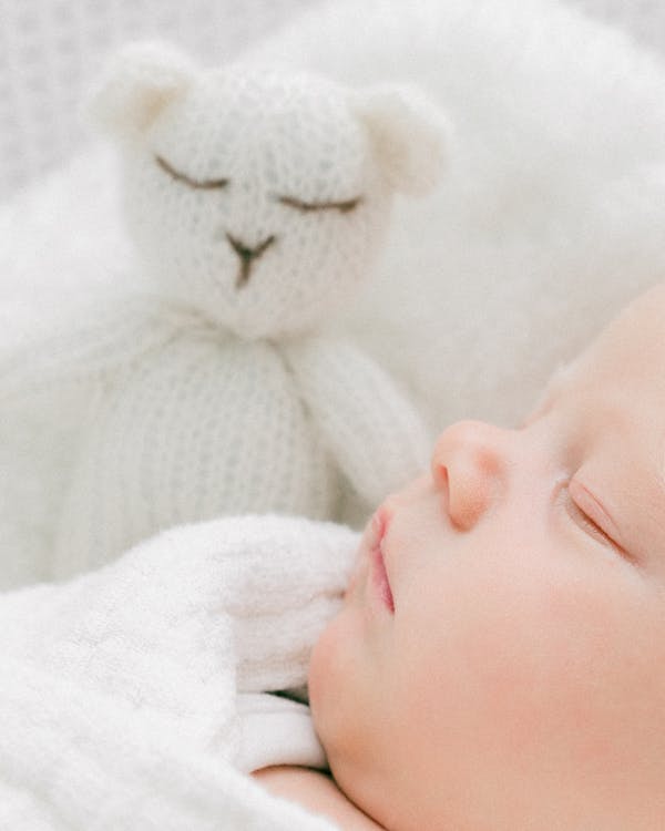 Closeup of a Baby Face Sleeping Next to a Yarn Teddy Bear Free