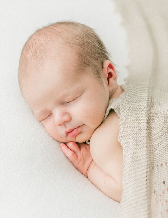 Free A serene and tender image of a newborn baby peacefully sleeping, partially wrapped in a delicate knit blanket. Stock Photo