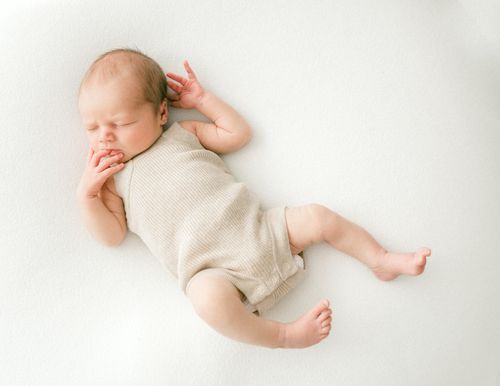 Free A serene newborn baby sleeping peacefully in a beige romper during a studio shoot. Stock Photo