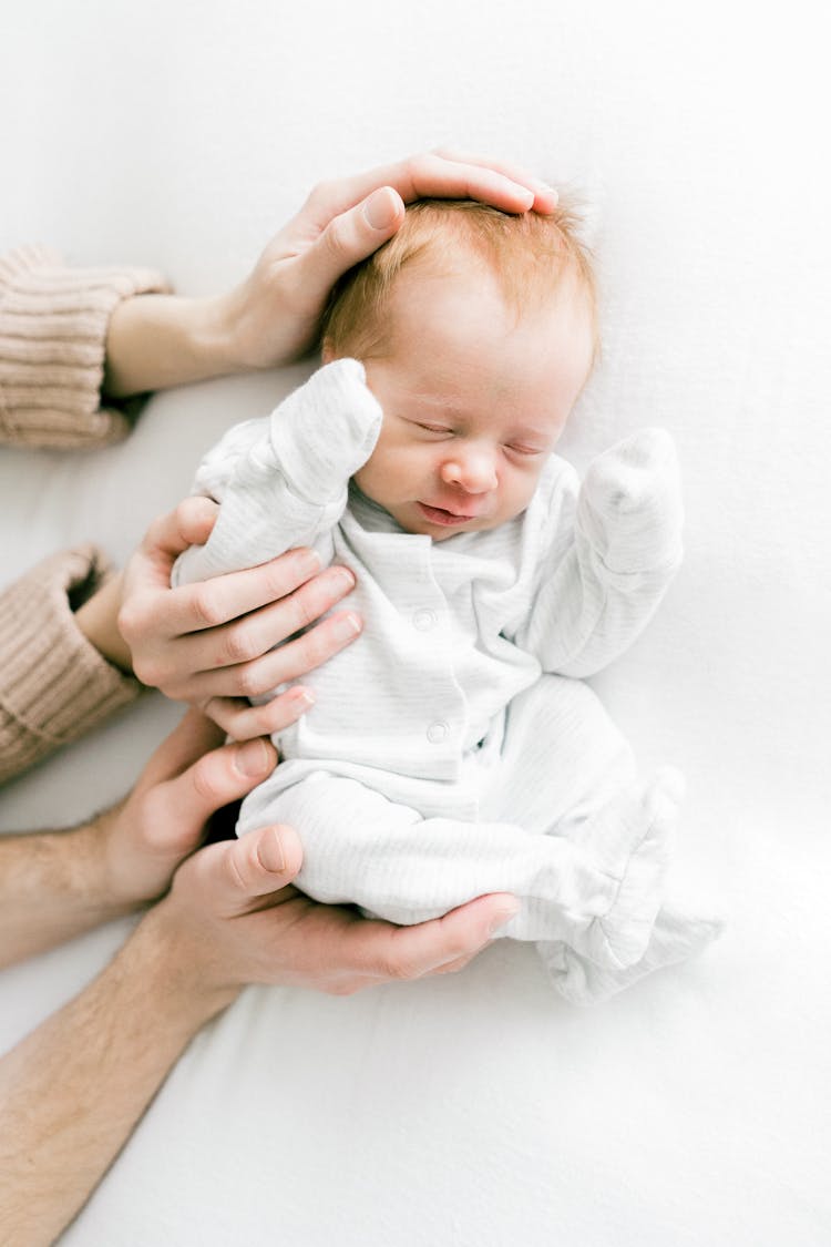 Mother And Father Hands Holding Sleeping Baby