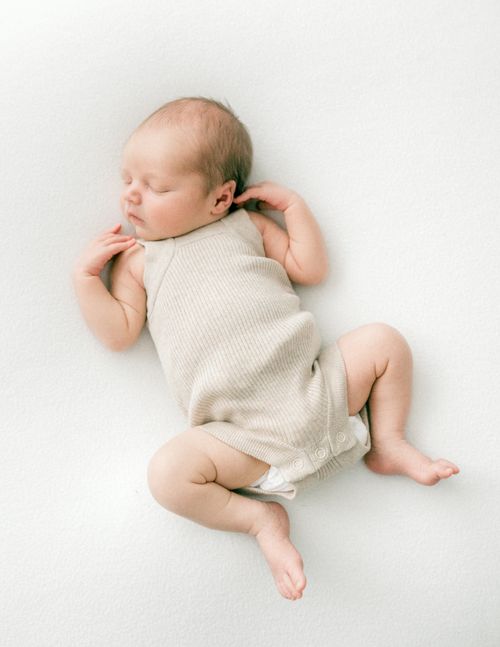 Free A serene sleeping baby in a neutral onesie, lying on a simple soft white background, captured from above. Stock Photo