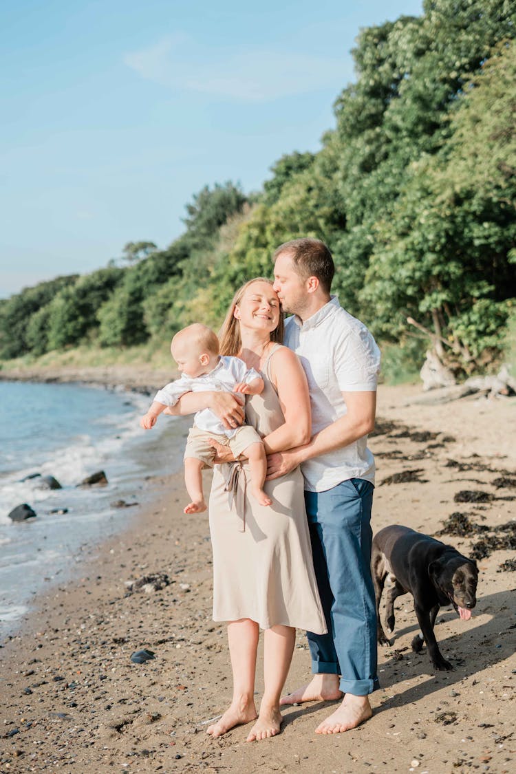 Couple Kissing And Holding Baby On Beach