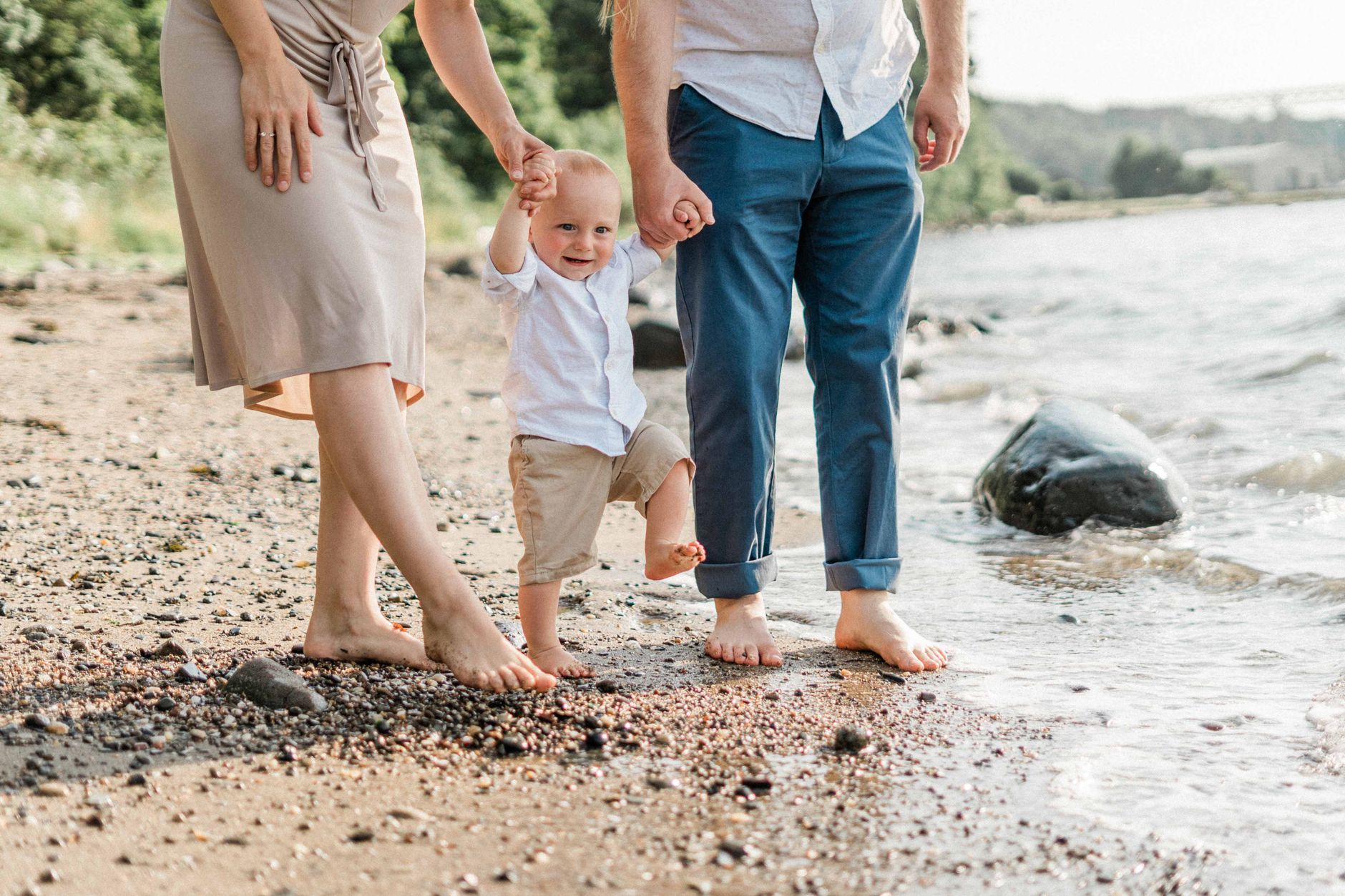 A family holding hands with their toddler boy at the beach, enjoying a sunny day.