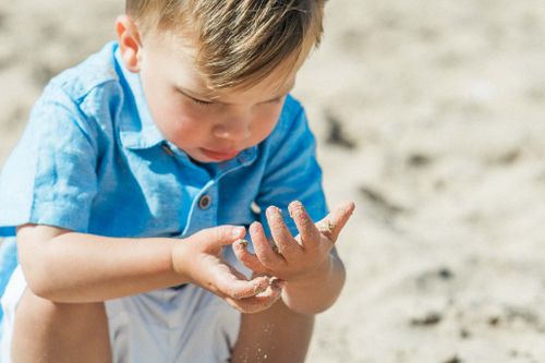 Free A young child in a blue shirt playing with sand on a sunny summer day. Stock Photo