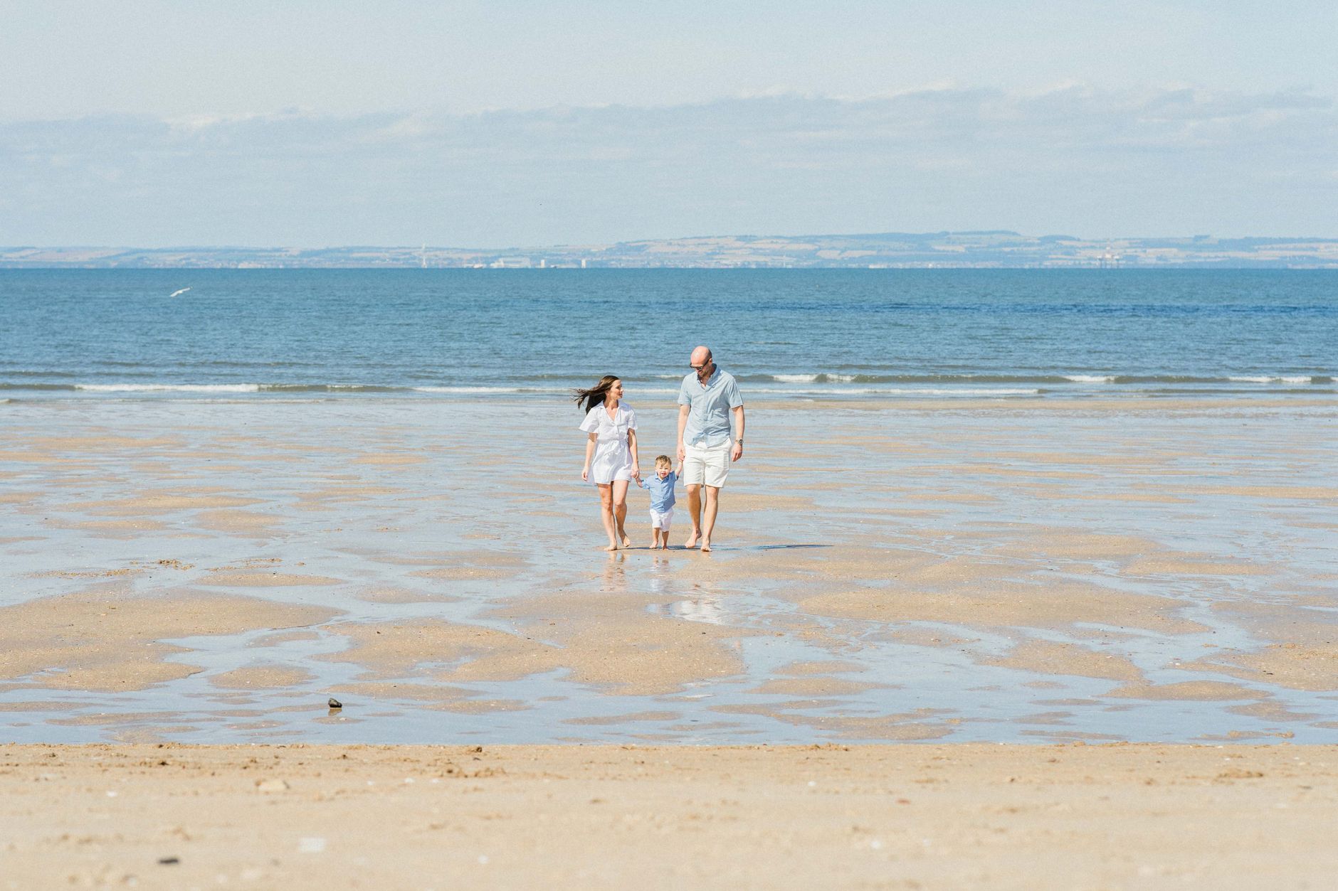 A joyful family walks hand in hand along the sandy beach on a sunny day.