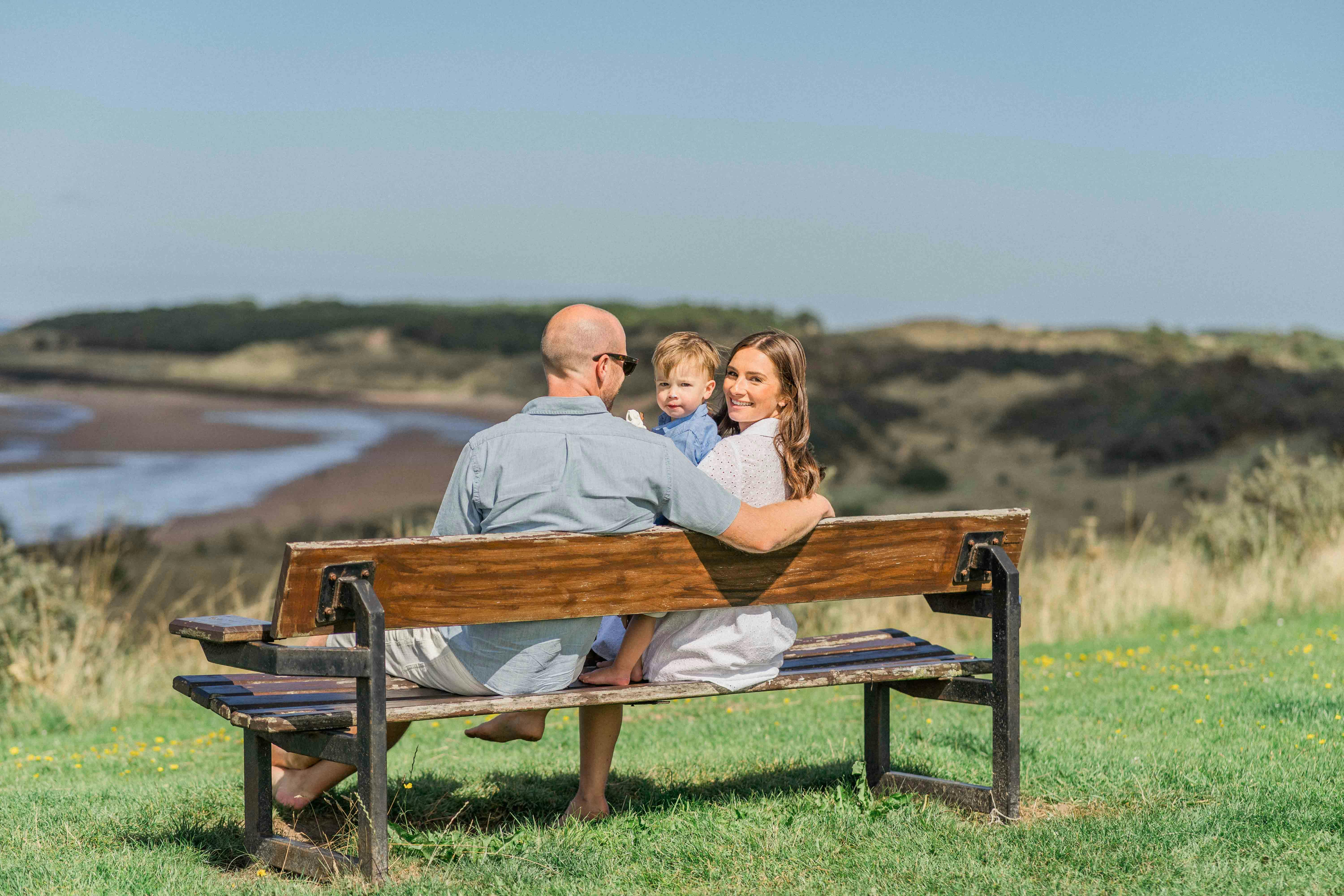 A family sitting on a bench overlooking a sunny beach, enjoying a relaxing day together.