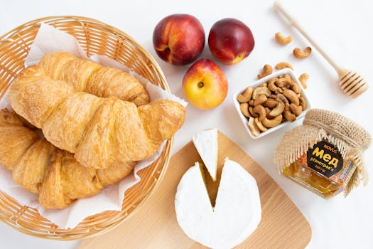 Flat lay of a French breakfast featuring croissants, camembert cheese, honey, and fresh fruits for a perfect start.