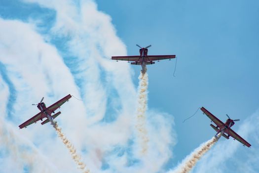 Three red planes execute stunning aerobatic maneuvers with smoke trails against a clear blue sky.