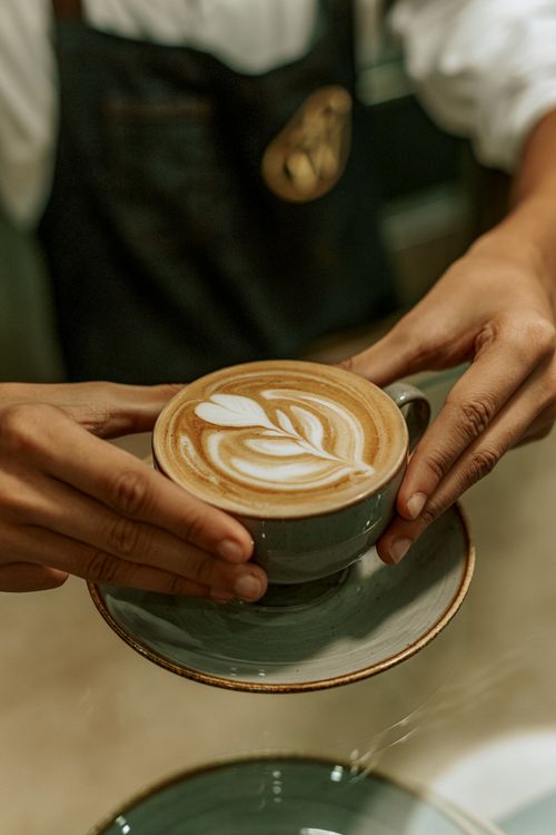 Free Close-up of a barista serving a latte with intricate leaf art at a café in Baku, Azerbaijan. Stock Photo