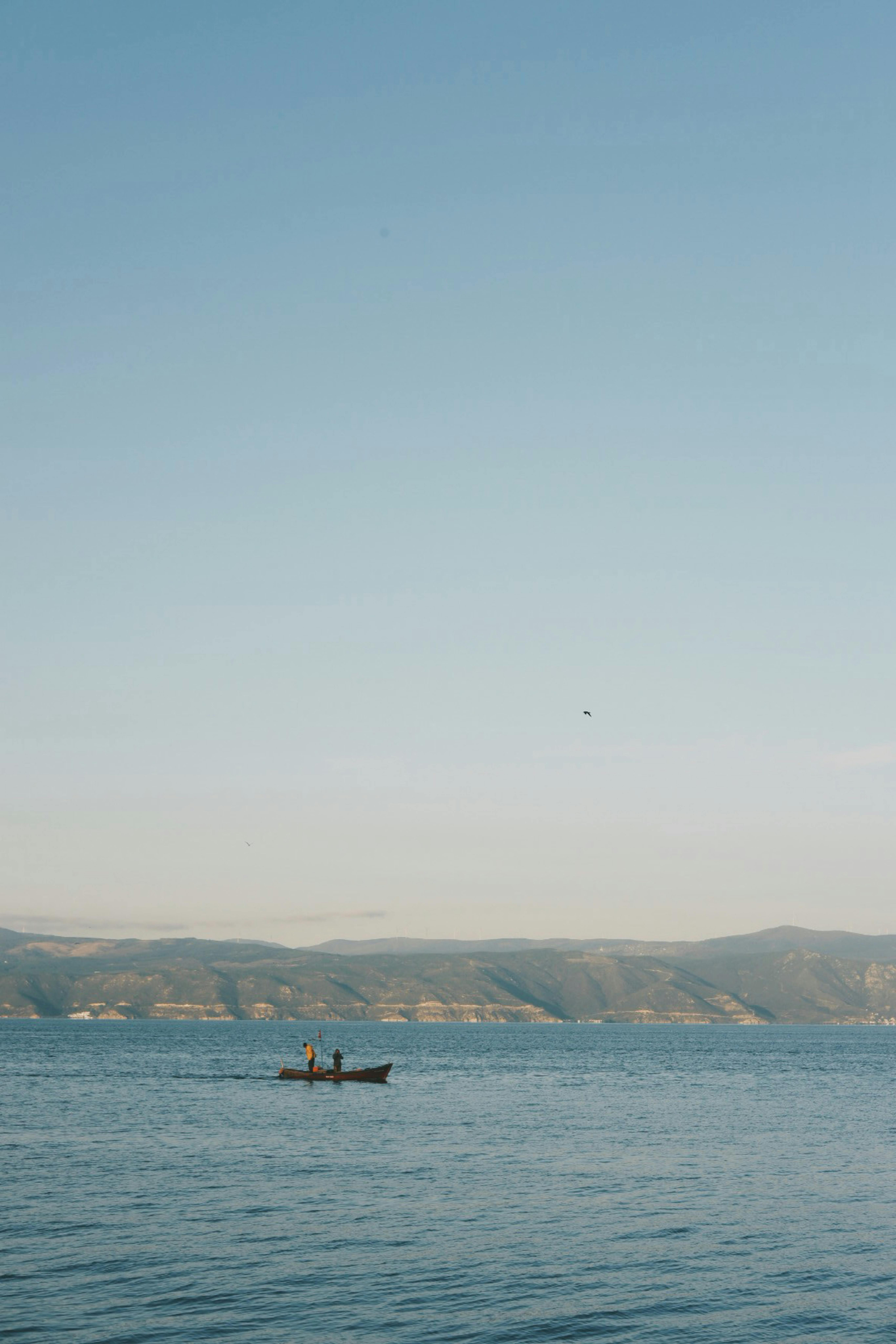 A calm scene of a small boat on a quiet lake against distant hills under a clear sky.