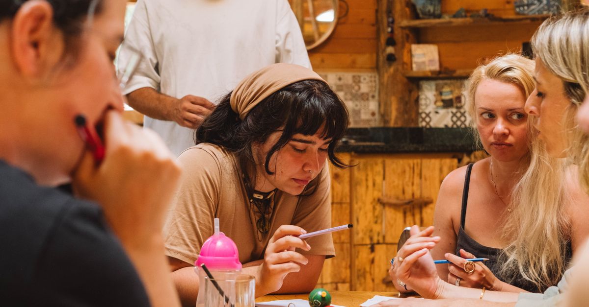 A team sitting around a table with notebooks, laughing and pointing at something on a whiteboard