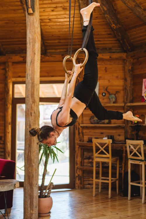 Free Woman practicing gymnastics on rings in a rustic wooden room, showcasing strength and balance. Stock Photo