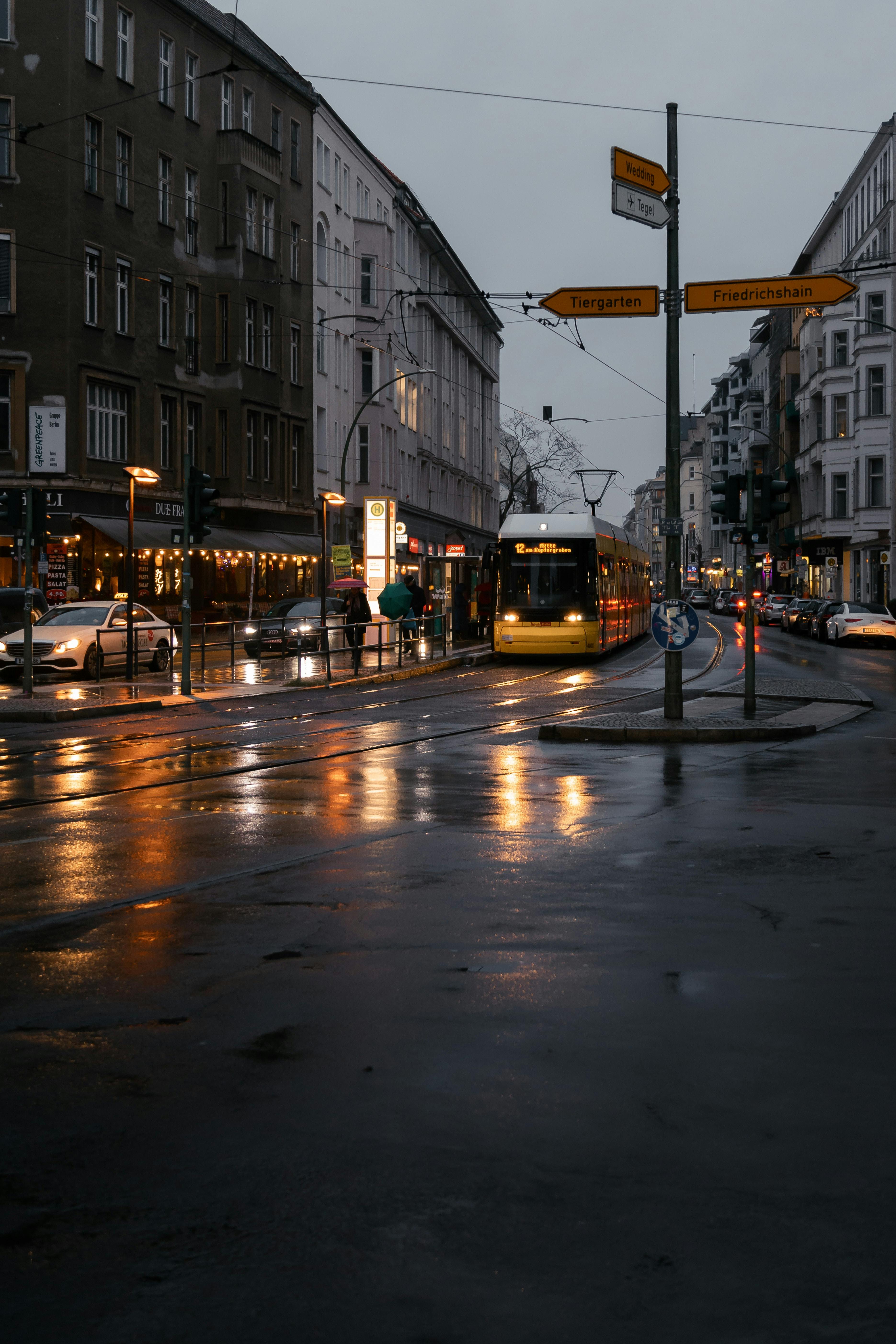 Moody street scene of a rainy evening in Berlin featuring a tram and vibrant city lights.