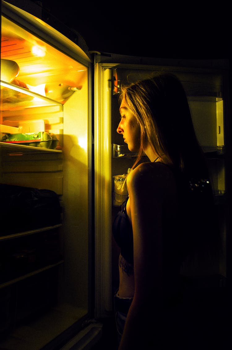 Woman Standing By Open Fridge In Darkness