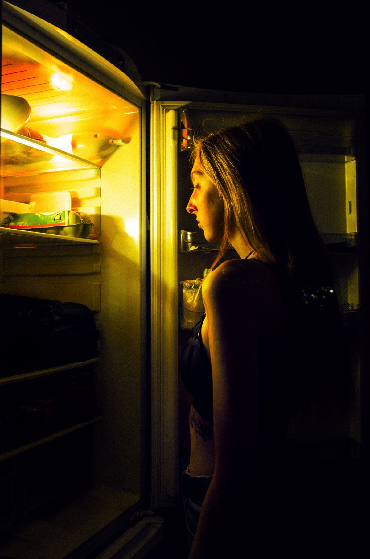 Woman standing at an open refrigerator at night