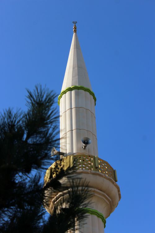 Free A majestic minaret rises elegantly against a clear blue sky, framed by tree leaves. Stock Photo