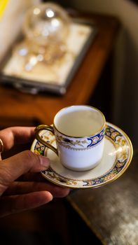 Elegant hand holding an intricately decorated porcelain cup on a saucer. Close-up shot indoors. — photo by tomris