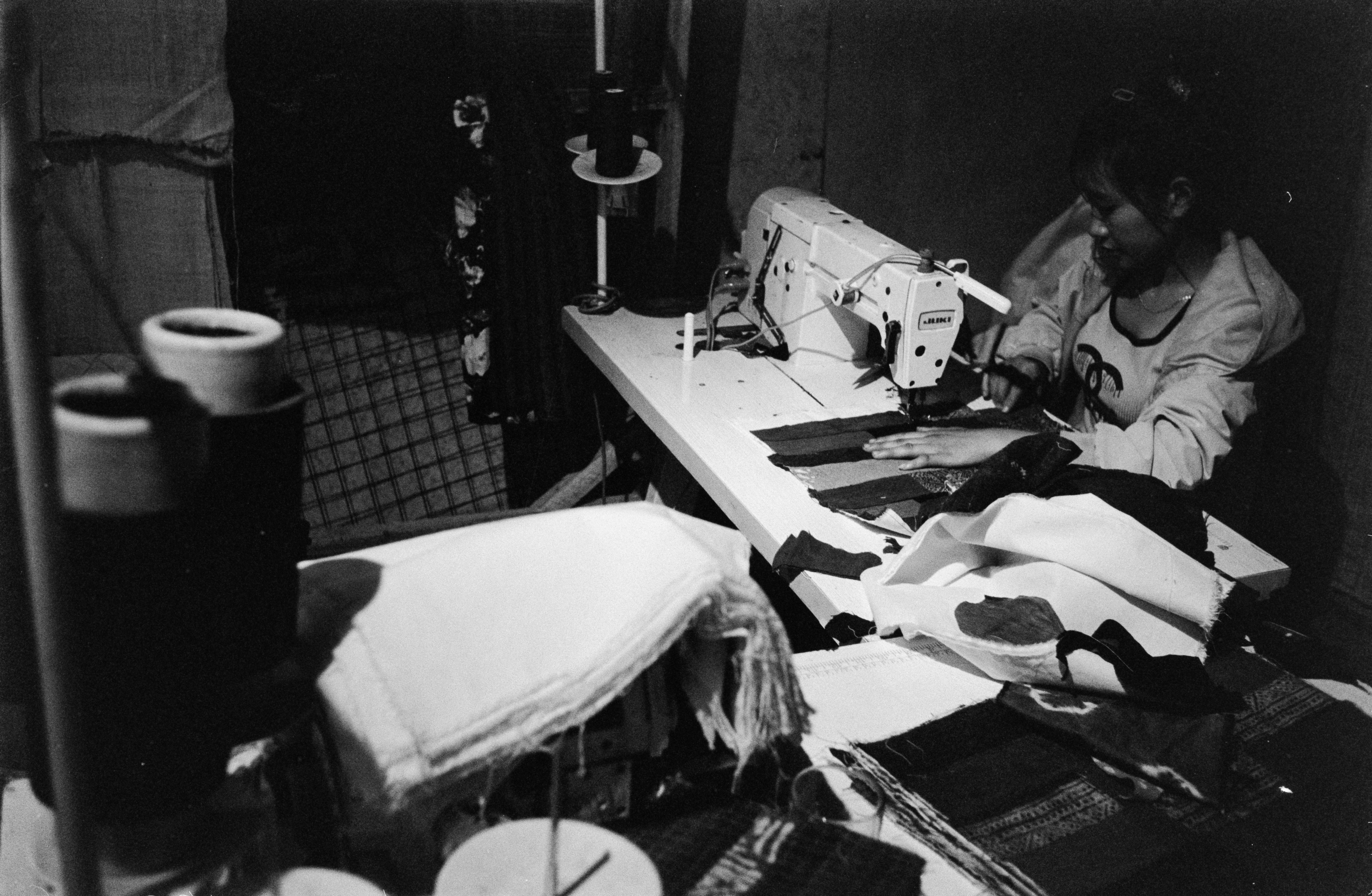 Tailor sitting and stitching garment at sewing machine in workshop showing tailoring order in progress