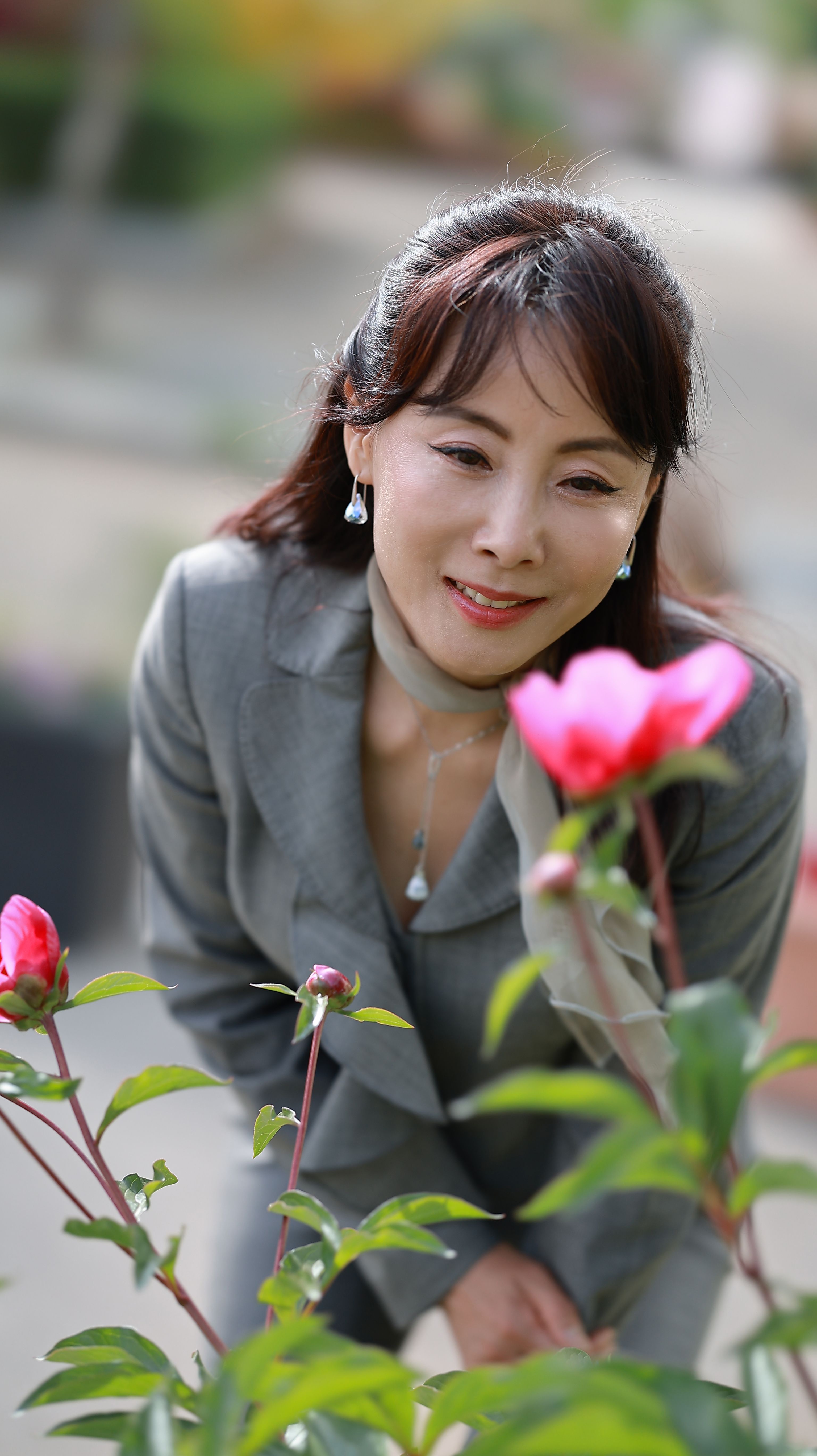 Woman in business attire admiring pink flowers in a garden setting.