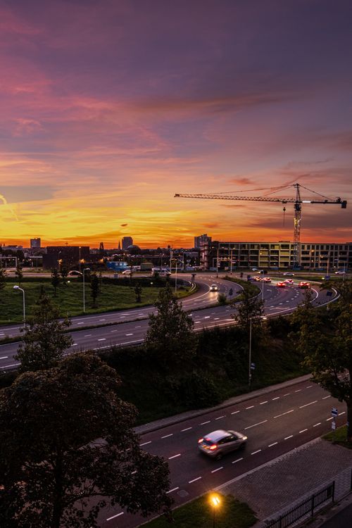 Free A beautiful urban cityscape showcasing roads, a crane, and sunset sky. Stock Photo