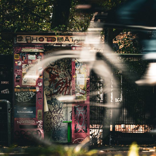 A graffiti-covered photo booth in Hamburg with a blurred bicycle passing by, capturing urban vibe.