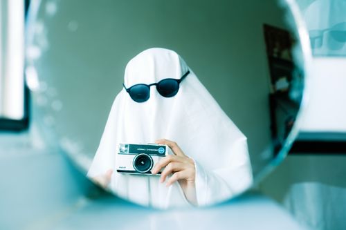 Free A funny image of a ghost costume with sunglasses taking a selfie in a mirror using a vintage camera. Stock Photo