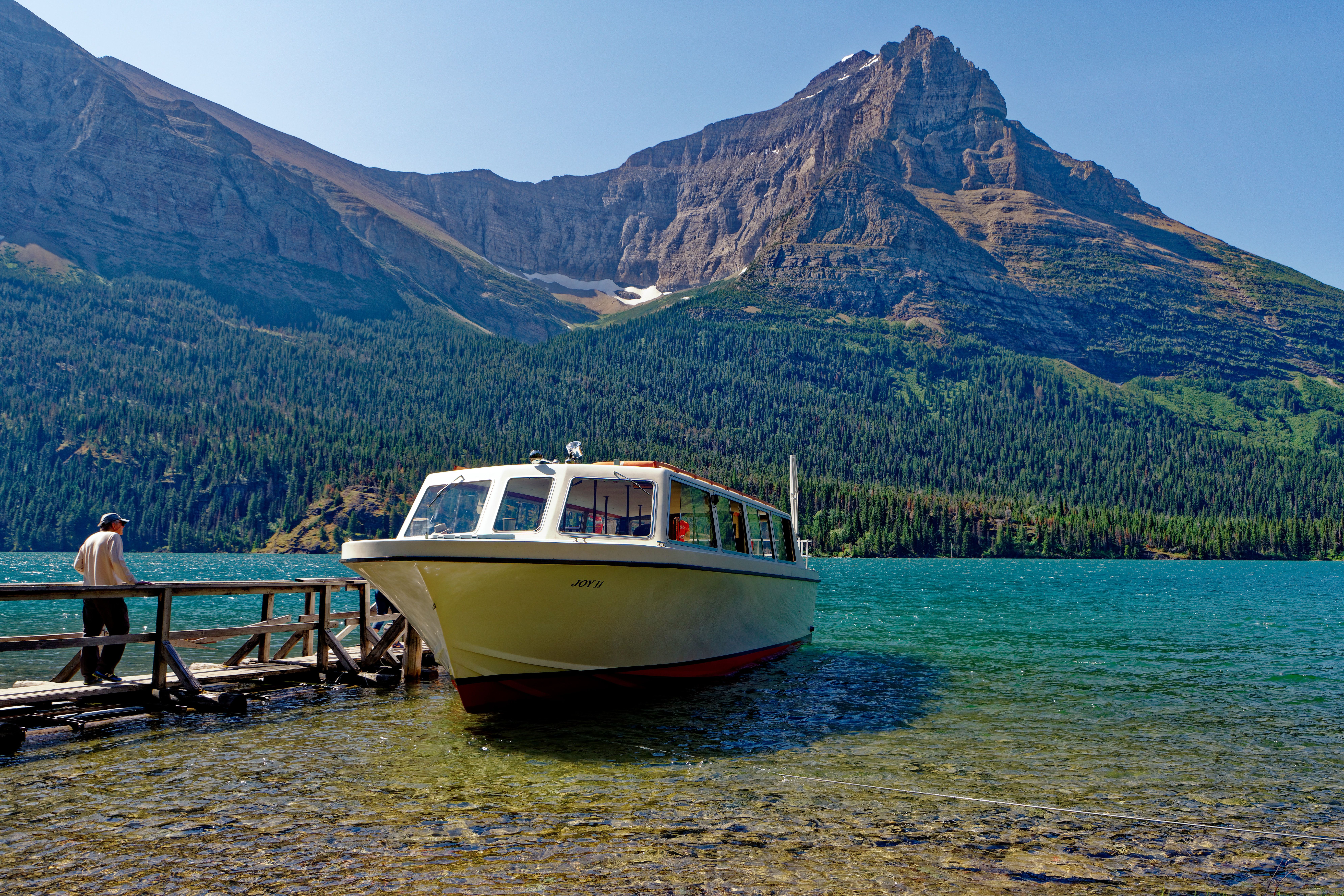 A tranquil scene with a moored boat at a lakeside, surrounded by majestic mountains and clear blue water.