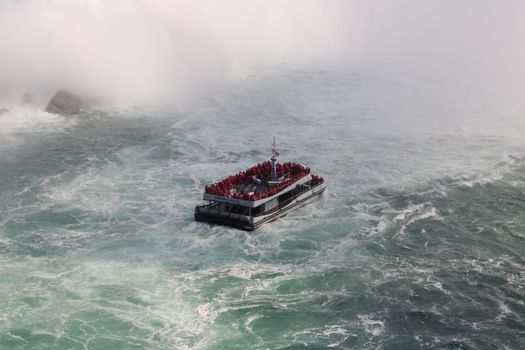 Aerial view of a crowded tourist ferry navigating the misty waters near Niagara Falls, Canada.