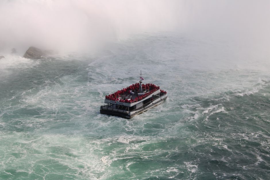 Niagara Falls Small Group Tour w/Helicopter and Maid of the Mist - Aerial view of a crowded tourist ferry navigating the misty waters near Niagara Falls, Canada.