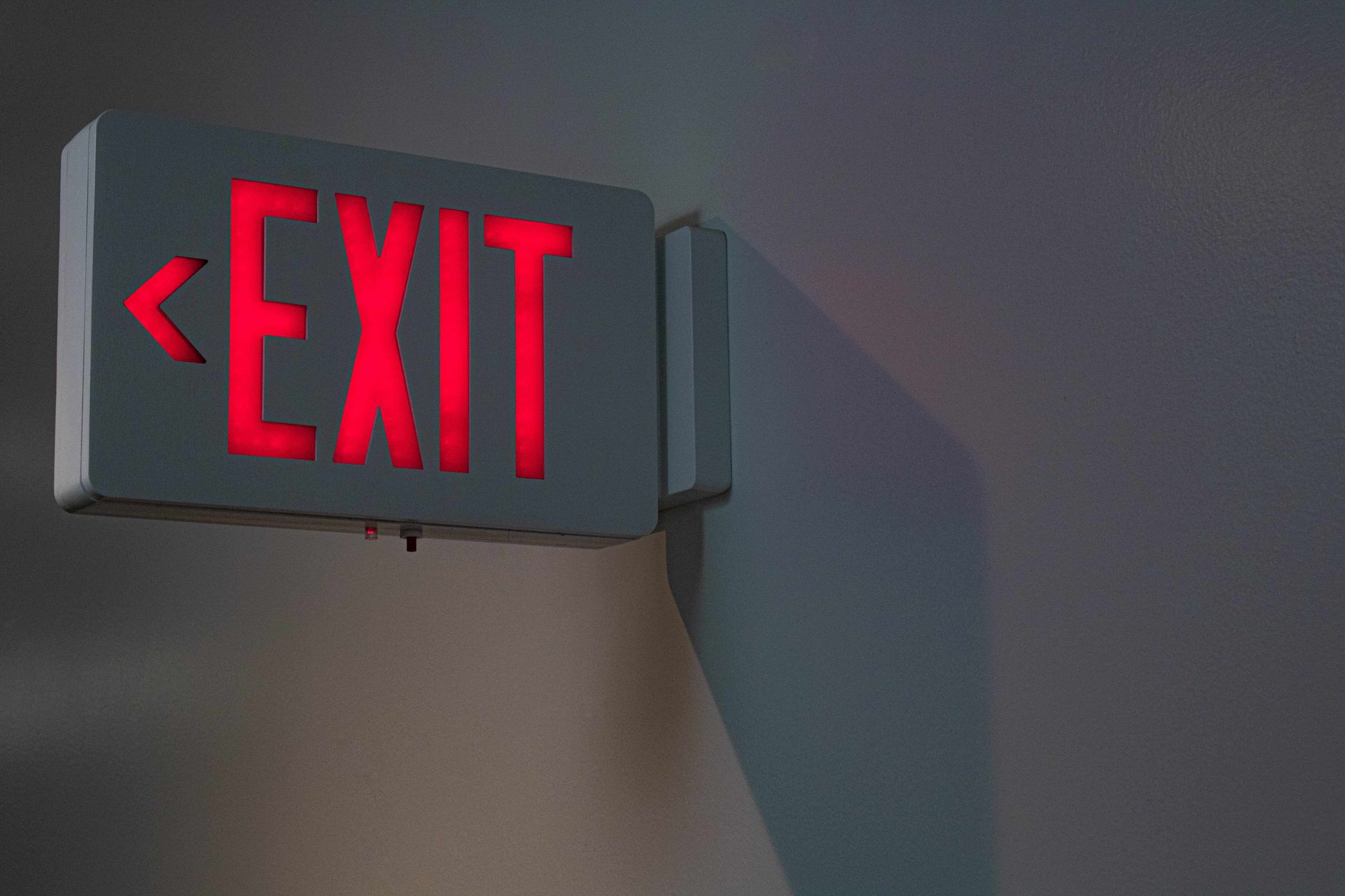 Close-up of a lit red exit sign on a gray wall, ideal for emergency and safety themes.