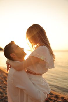 A couple shares a romantic embrace on the beach with a beautiful sunset backdrop.