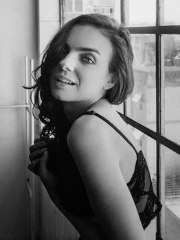 Black and white portrait of a woman in lingerie by a window with natural light.