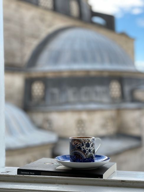 A detailed Turkish tea cup on a book with a blurred mosque background, highlighting cultural essence.