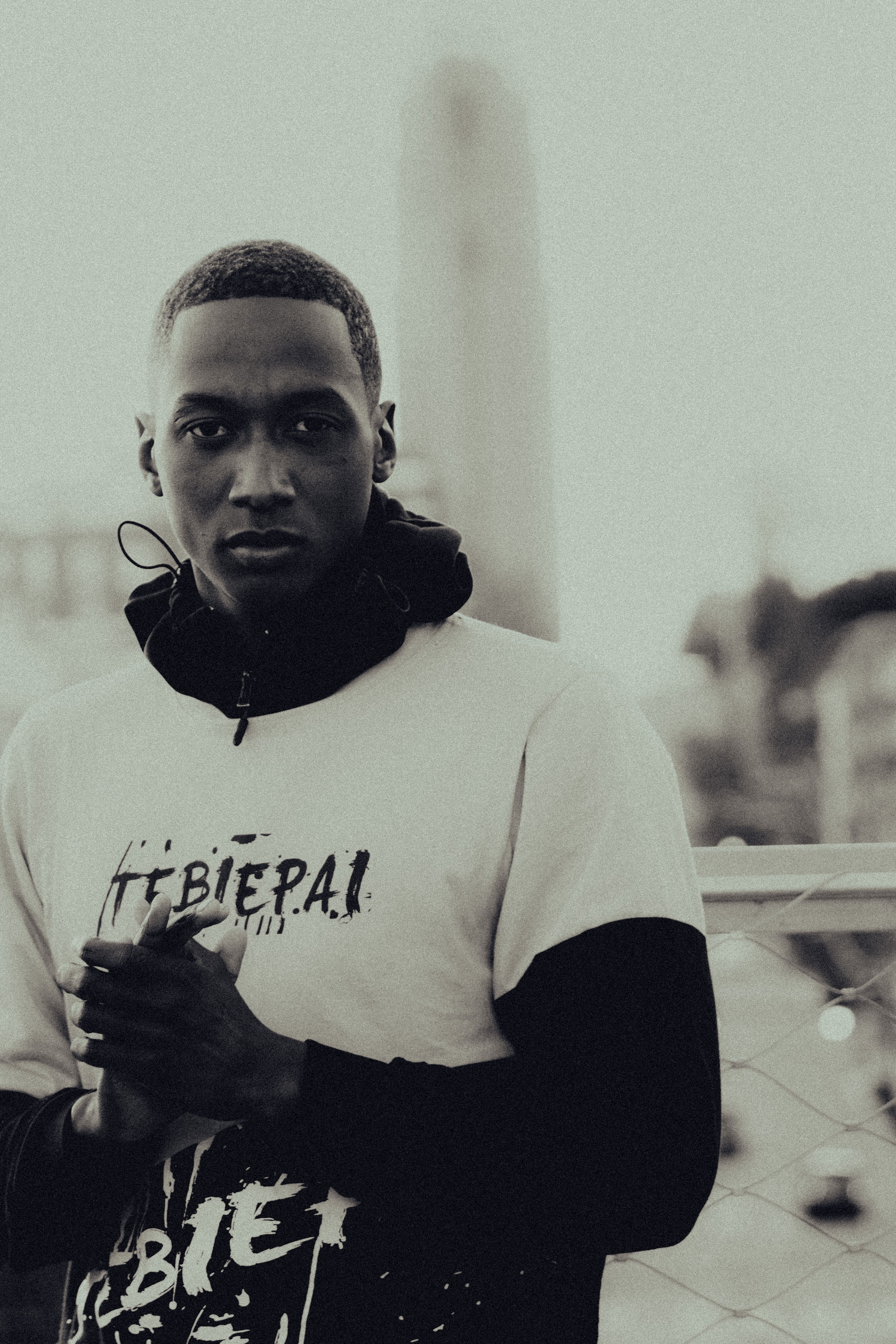 Black and white portrait of a young man in urban setting, showcasing fashion style.