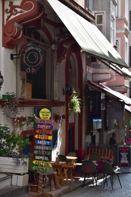 Free Cozy urban café on a vibrant street corner with inviting outdoor seating and colorful signage. Stock Photo