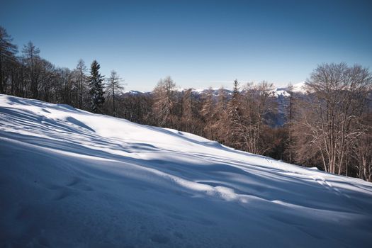 A peaceful winter scene with snow-covered hills and distant mountains under a clear blue sky.