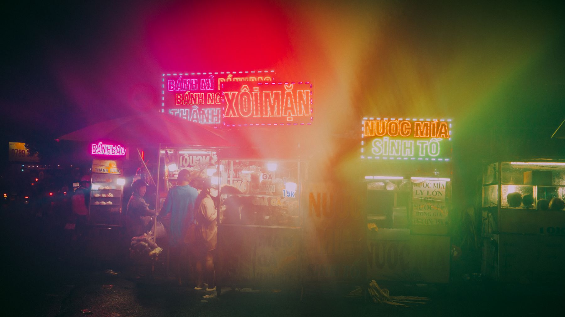 Neonbeleuchtete Streetfood-Stände schaffen eine lebendige Atmosphäre auf einem belebten Nachtmarkt.